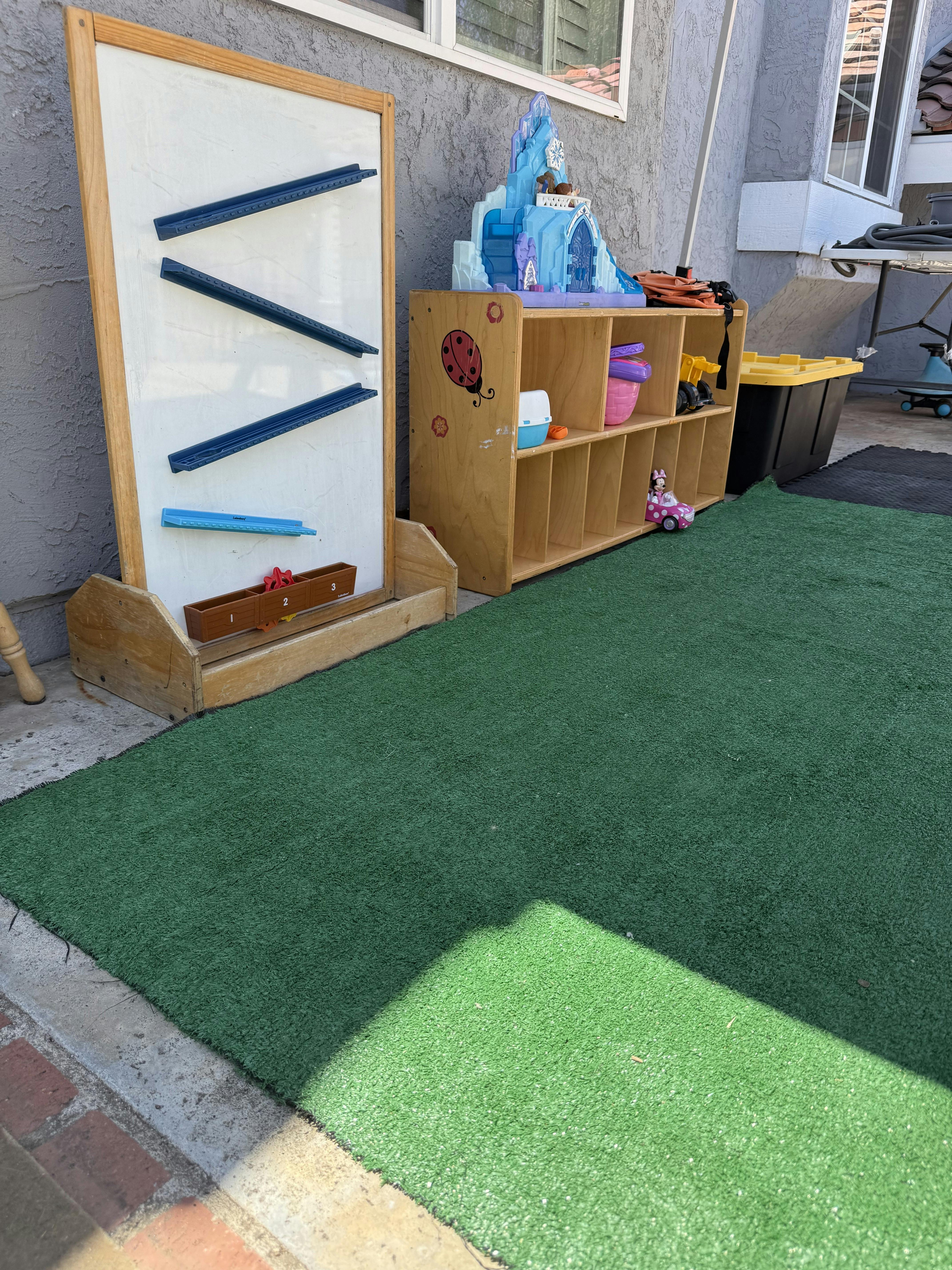 Play board and storage shelf with various toys on a green outdoor play mat