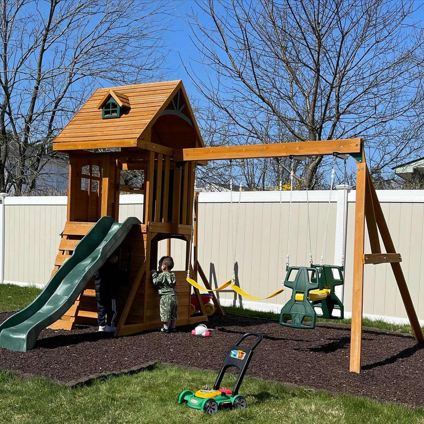 Child standing by a wooden playset with a slide and swings