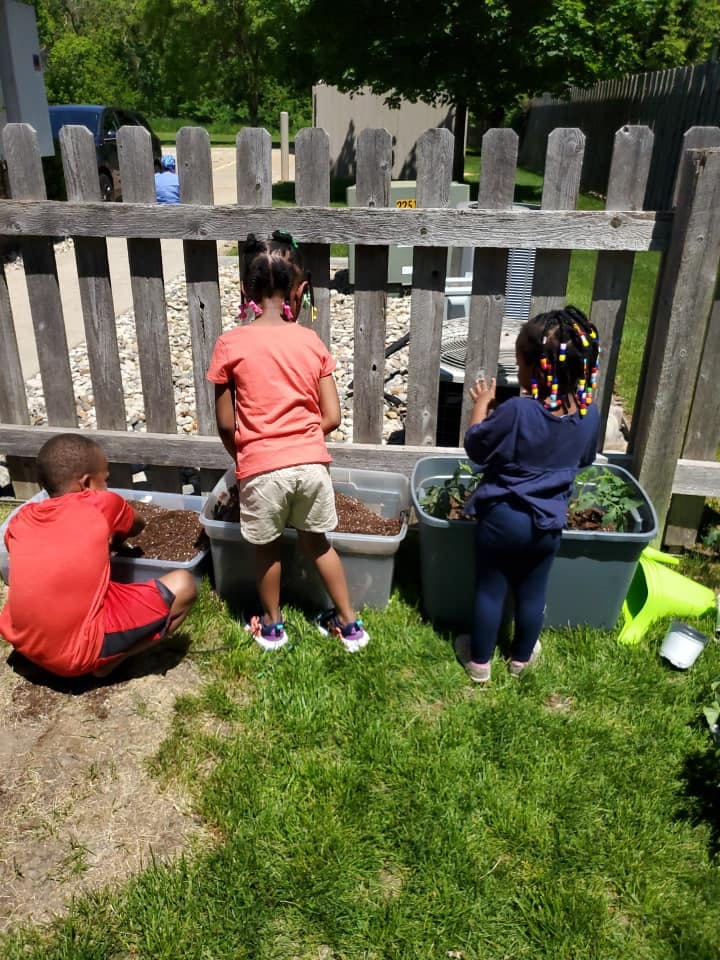 Three children planting in containers outdoors