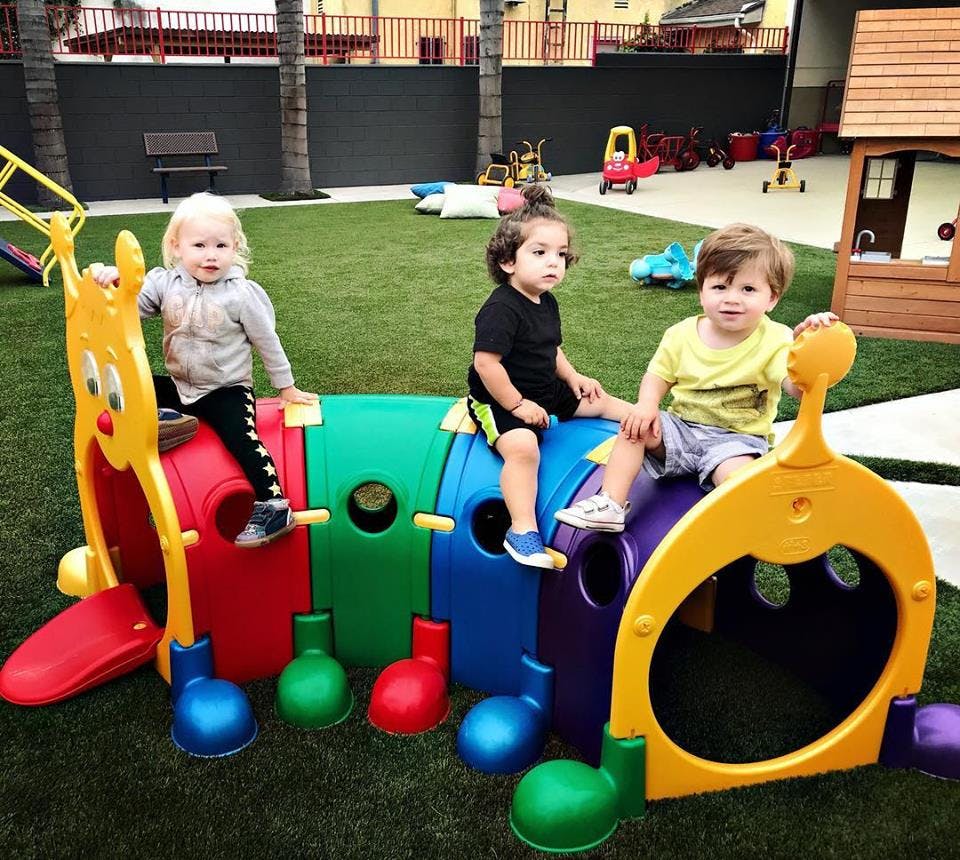 Three children playing on a colorful caterpillar-shaped playground climber