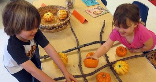 Two children playing tic-tac-toe with gourds and sticks on a grid of branches