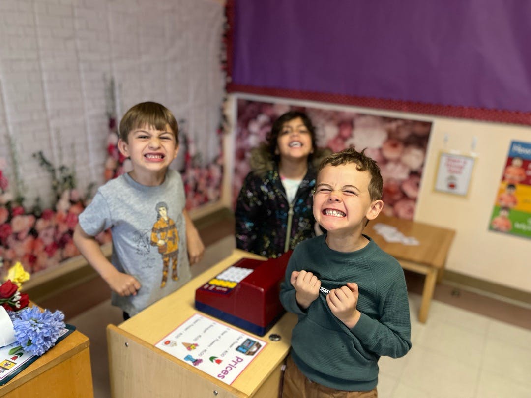 Three children smiling and looking at the camera in a classroom