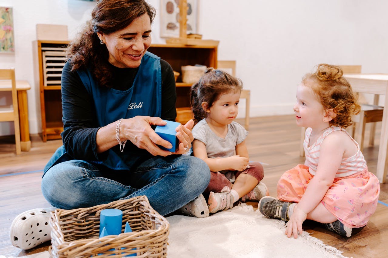 Person sitting on floor with two children, holding a blue block
