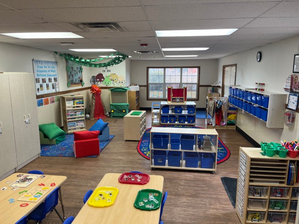 Classroom with wooden tables and chairs, storage shelves, and play areas