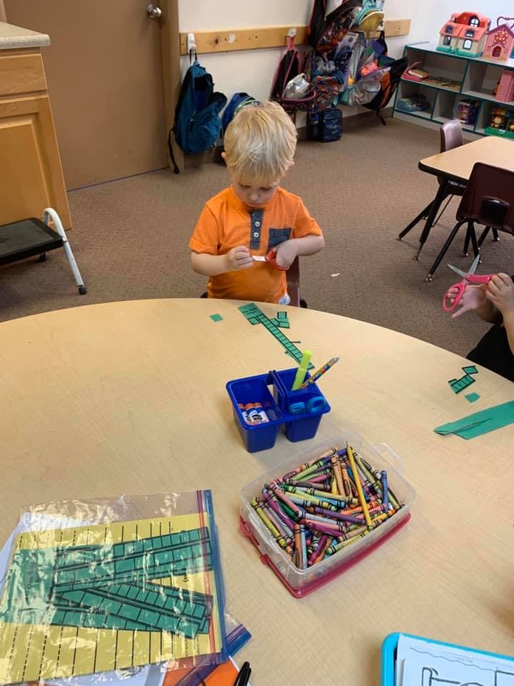 Child cutting paper at a table in a classroom