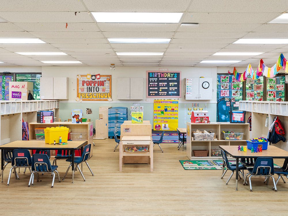 Empty preschool classroom with small tables and chairs, and a \"Poppin' into Preschool\" sign