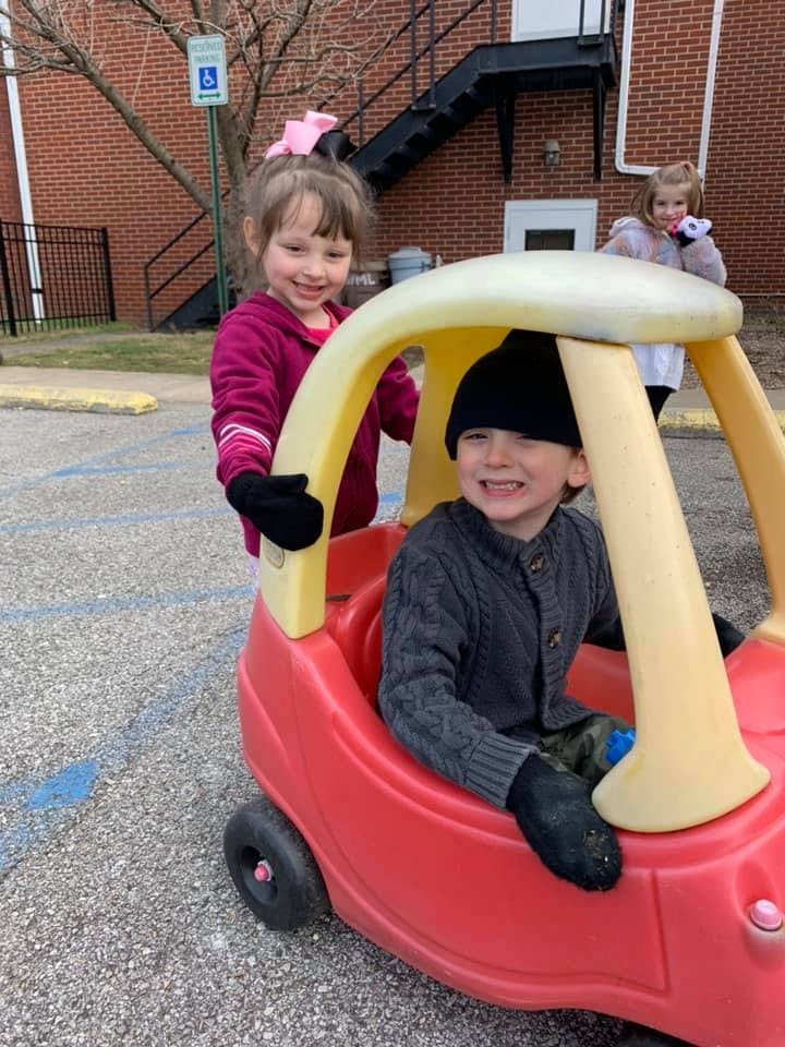 Child pushing another child in a toy car