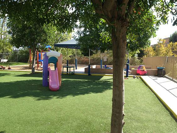 Playground with green turf, colorful slide, and shade umbrellas