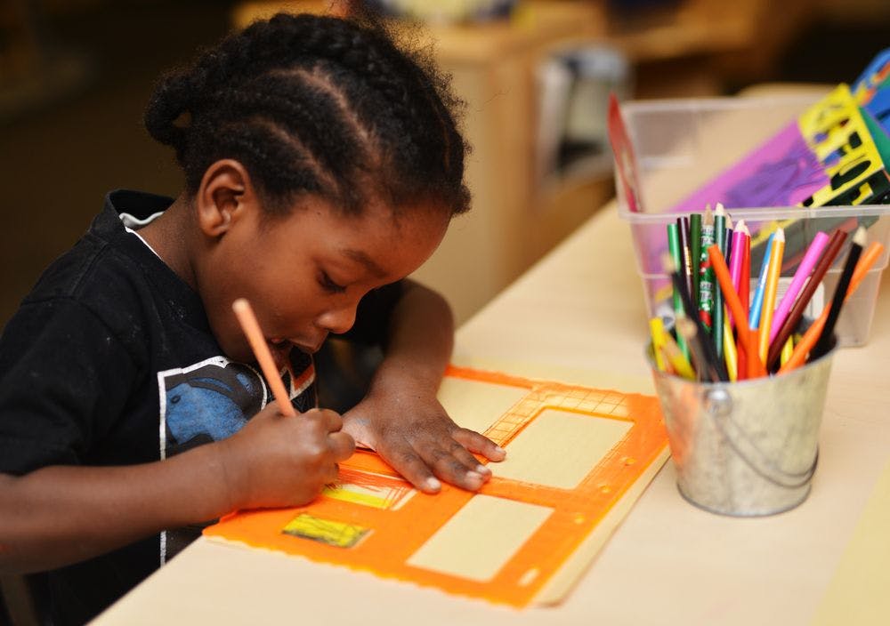 Child drawing on an orange stencil with a pencil