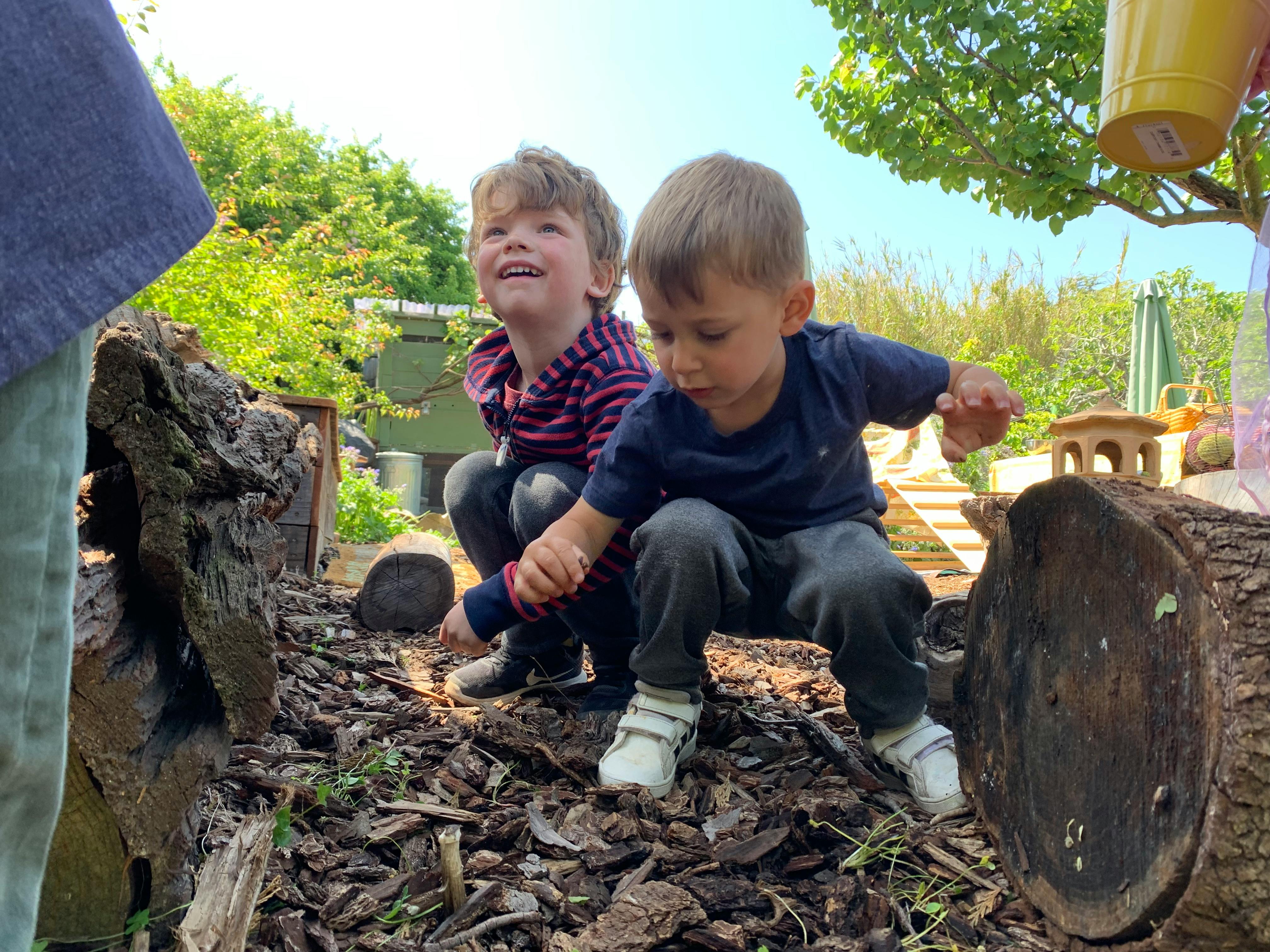 Two children crouching outdoors, one looking up and one looking down
