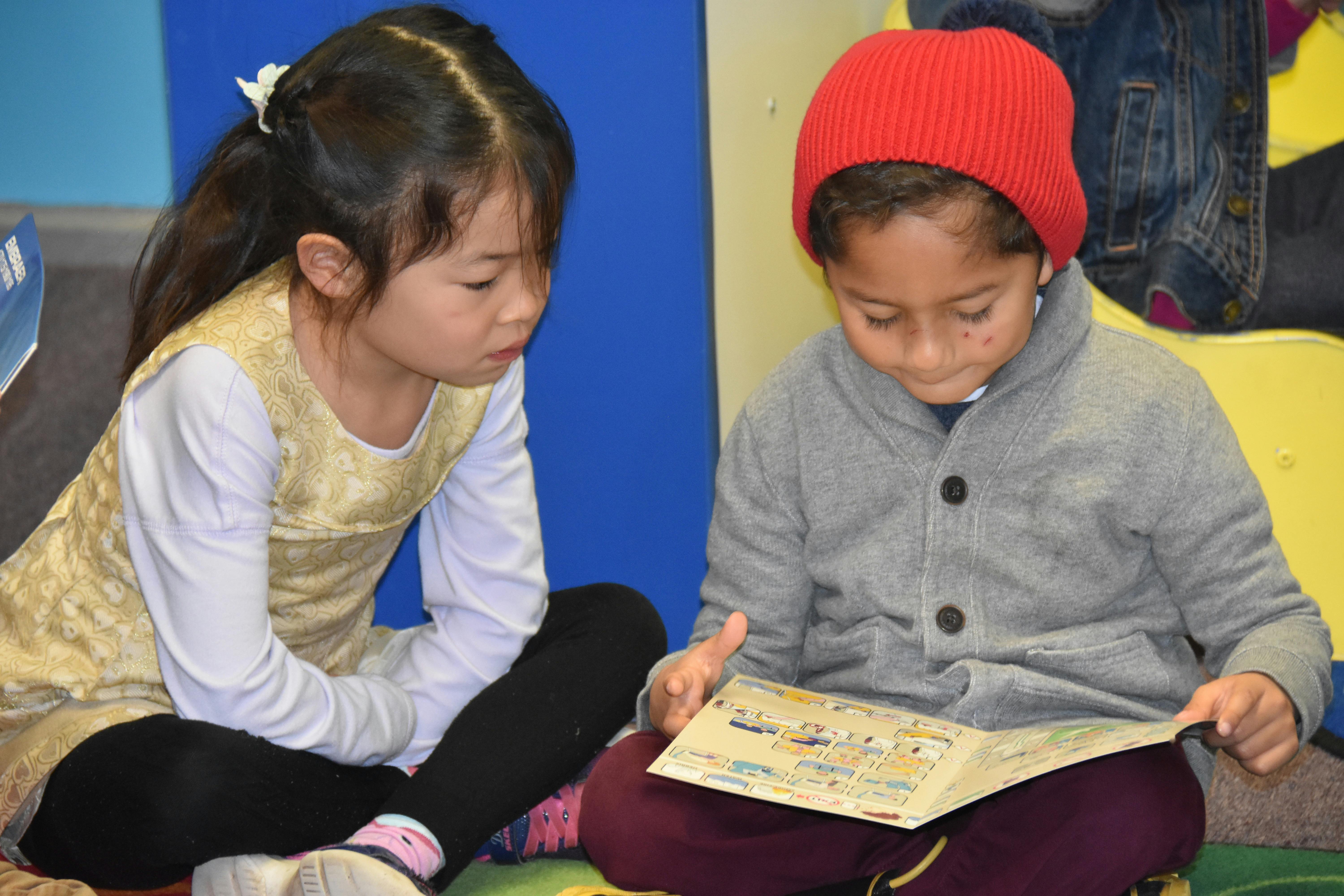Two children sitting on the floor looking at a book