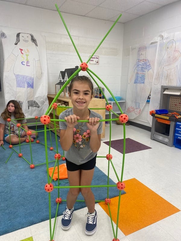 Child standing inside a green and orange fort structure in a classroom