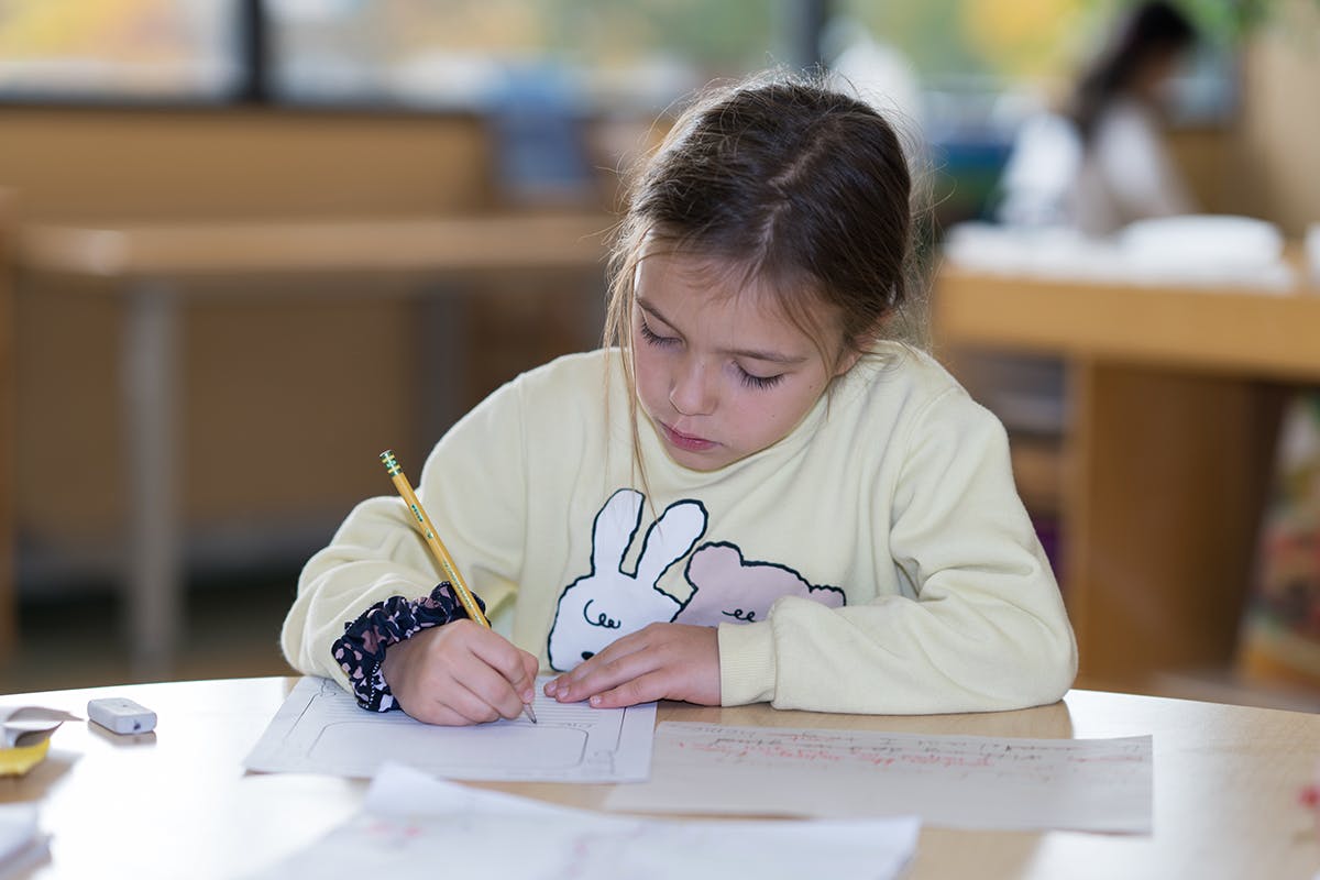 Child writing on paper with a pencil at a desk