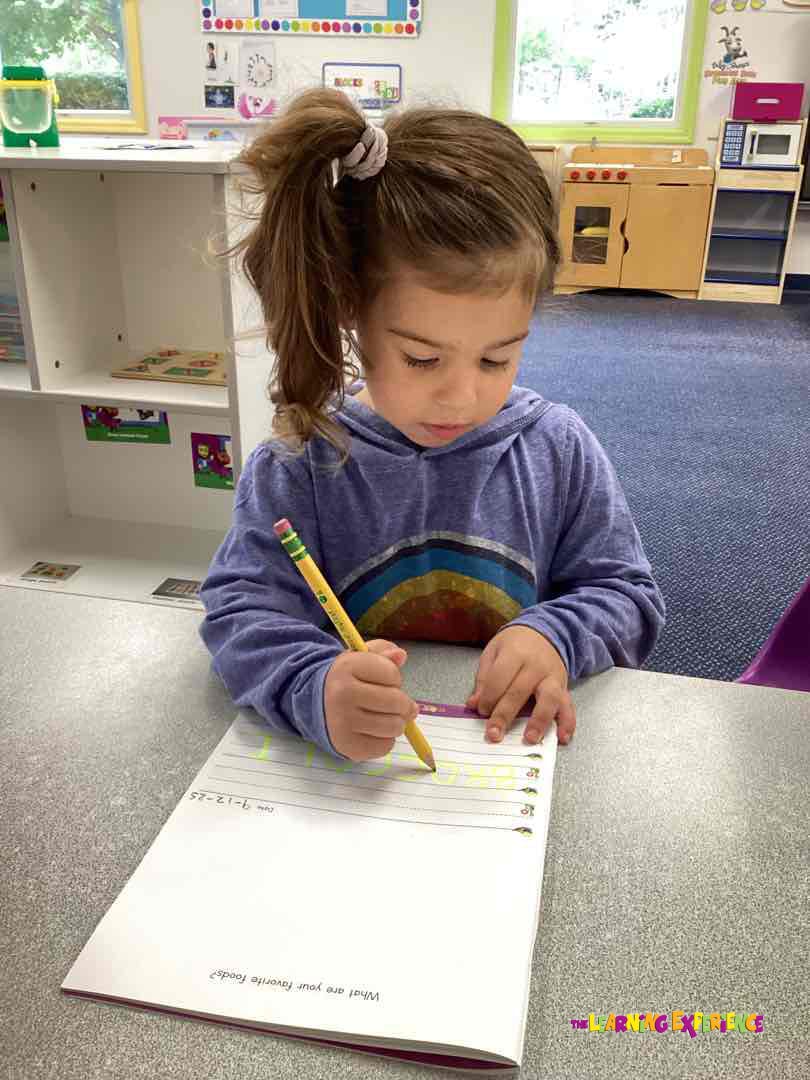 Child writing in a notebook with a pencil at a desk