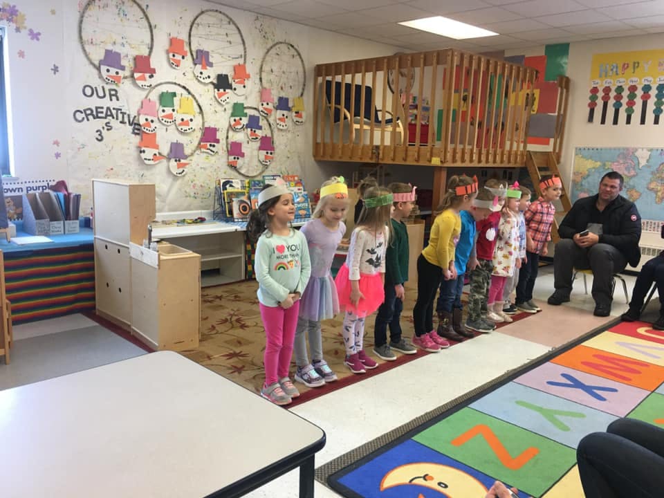 Children in a classroom standing in a line with an adult seated nearby
