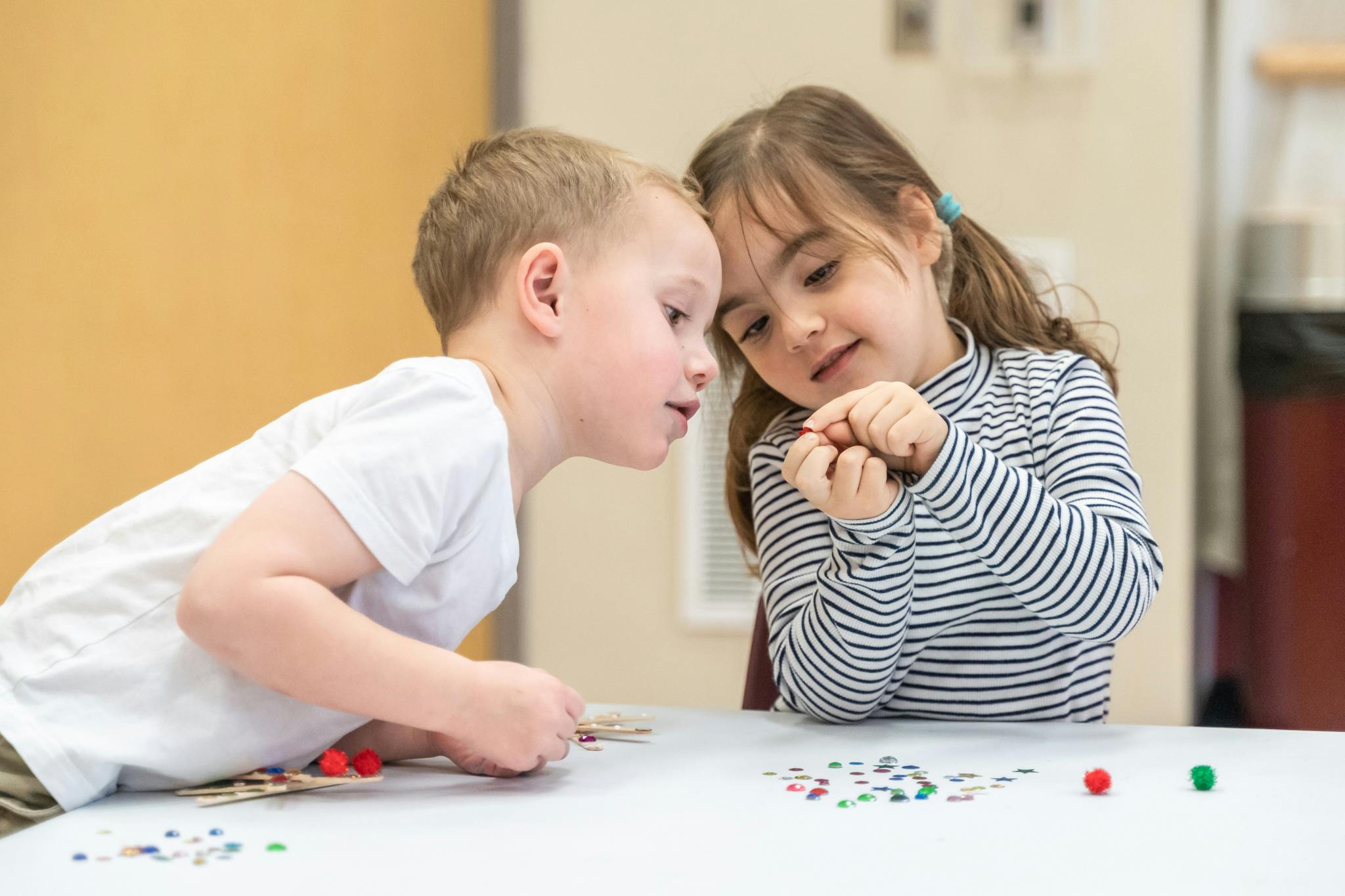 Two children leaning in close to look at small objects on a table