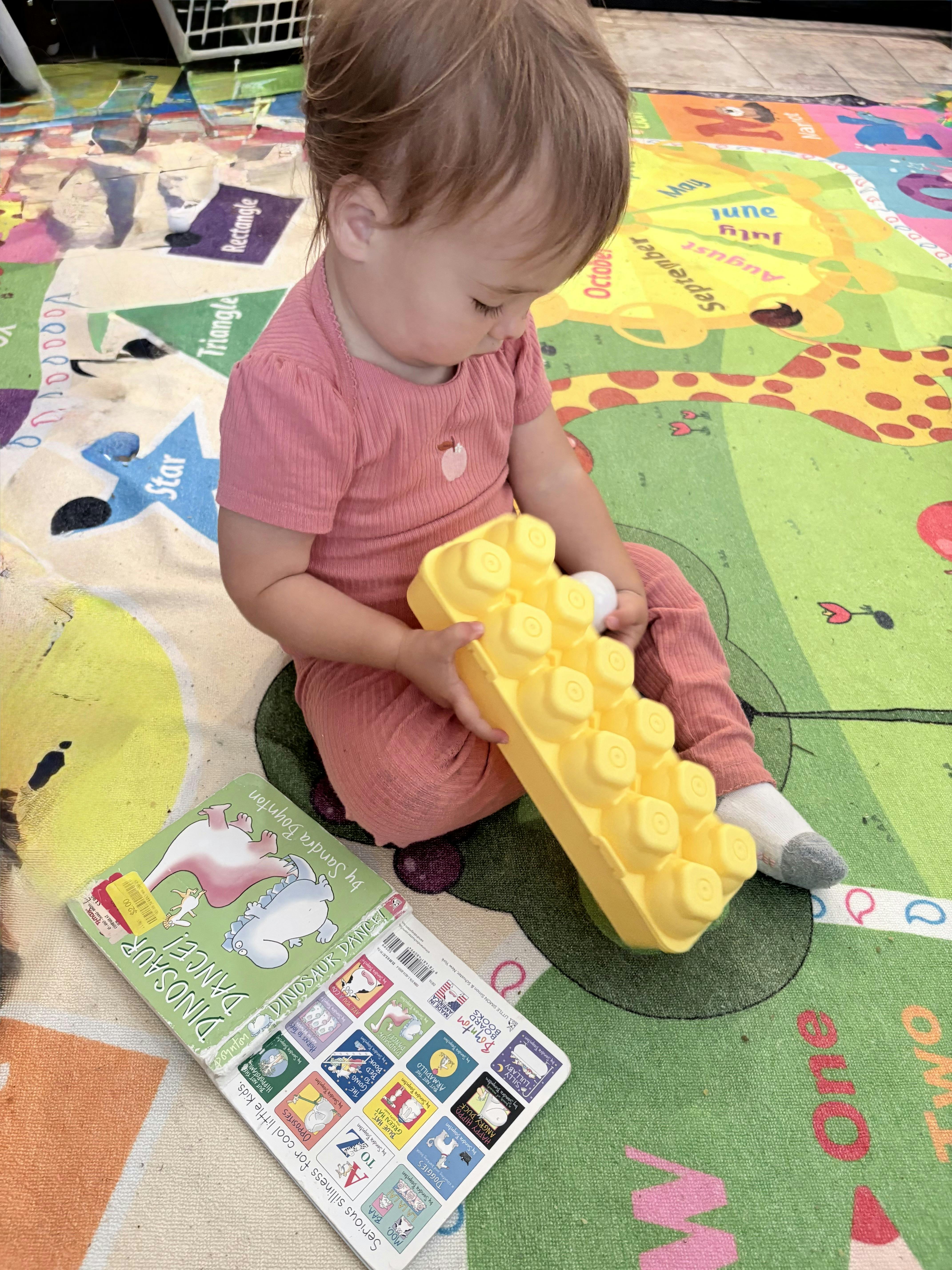 Child sitting on a play mat playing with a yellow egg carton and an egg carton