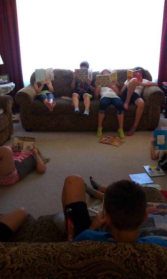 Several children reading books on a couch and floor