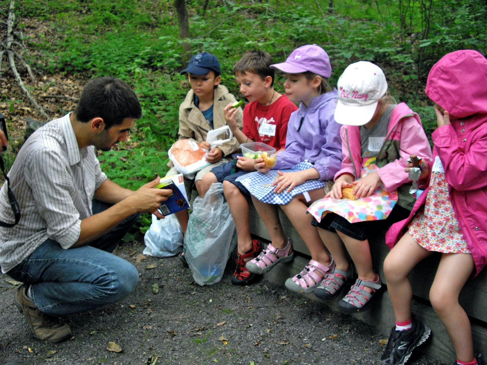 Person crouching with children sitting and eating outdoors