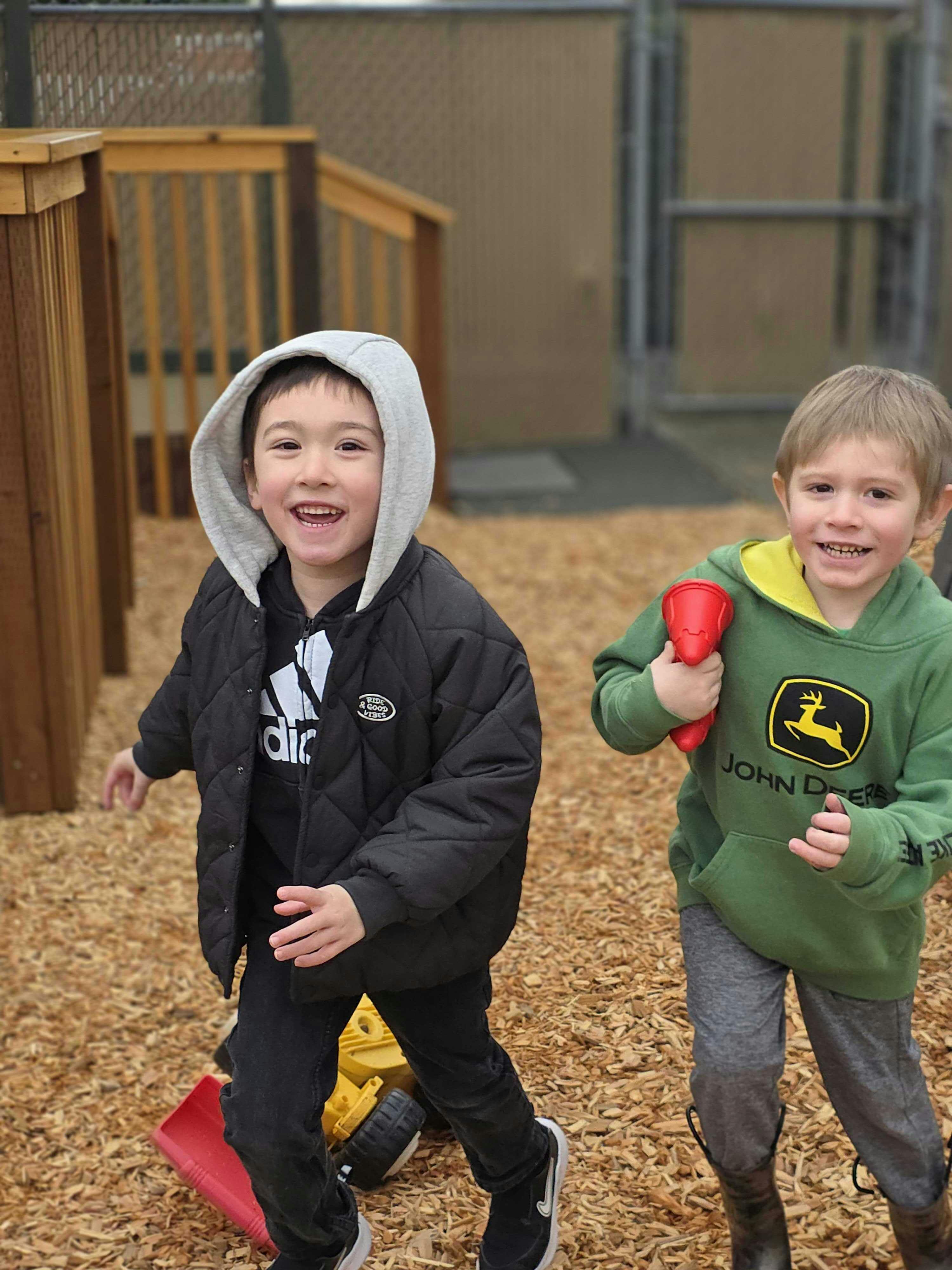 Two smiling children running together on wood chips at an outdoor playground