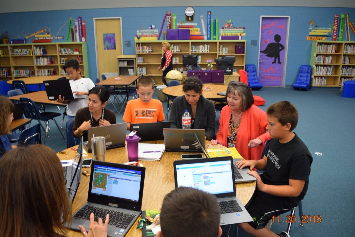 Adults and children working on laptops in a classroom