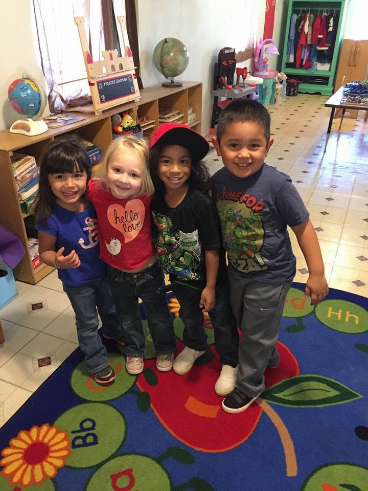 Four children standing together on a colorful rug in a classroom