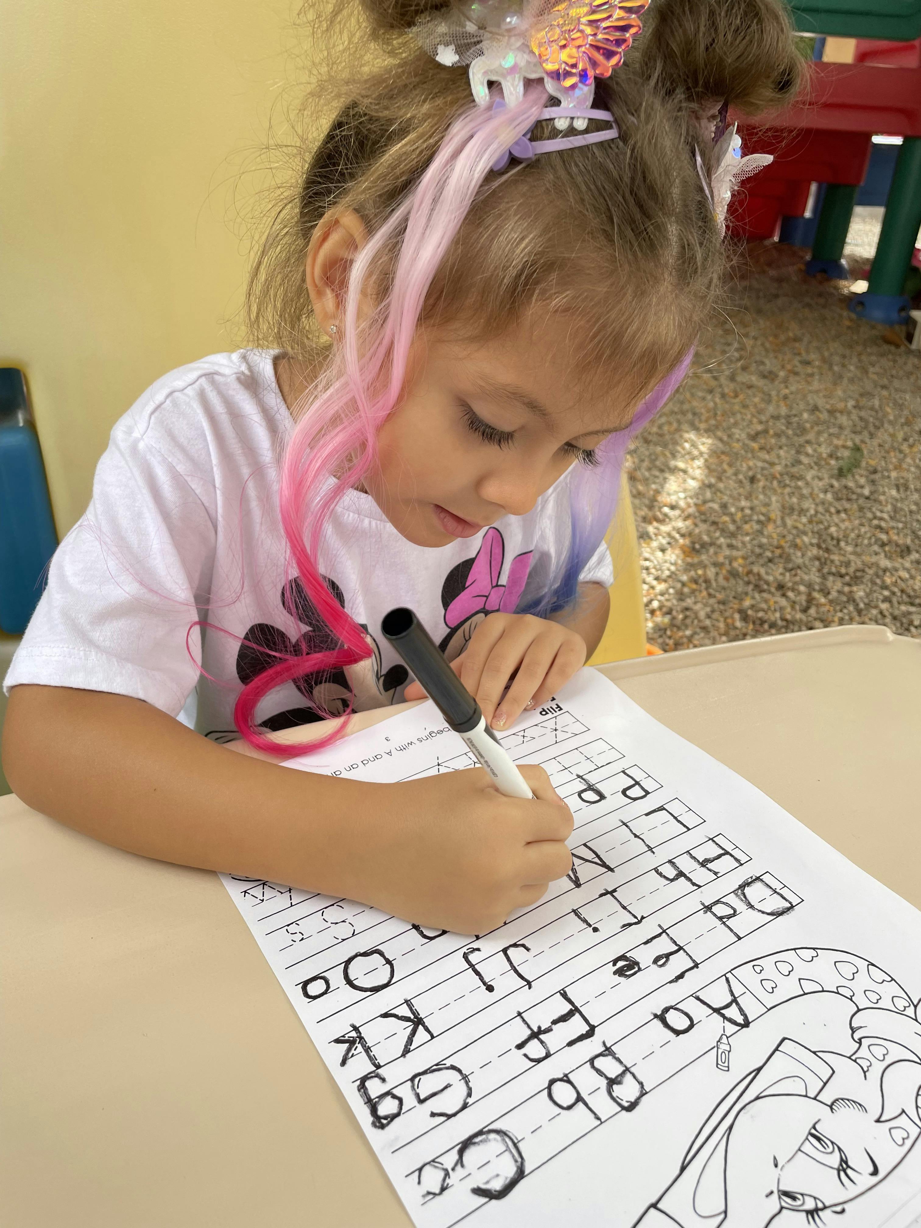 Child writing letters on a worksheet with a marker