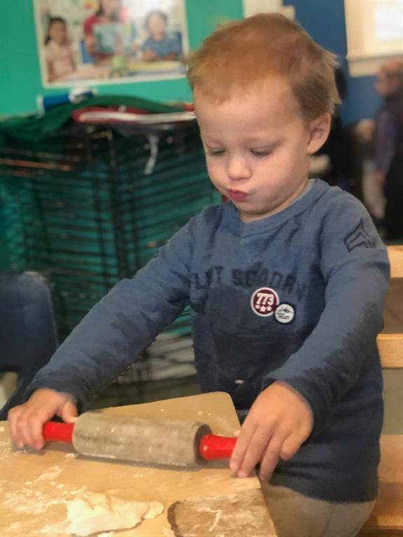 Child using a rolling pin on dough