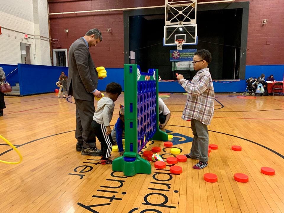 Adult and children playing a large Connect Four game in a gym