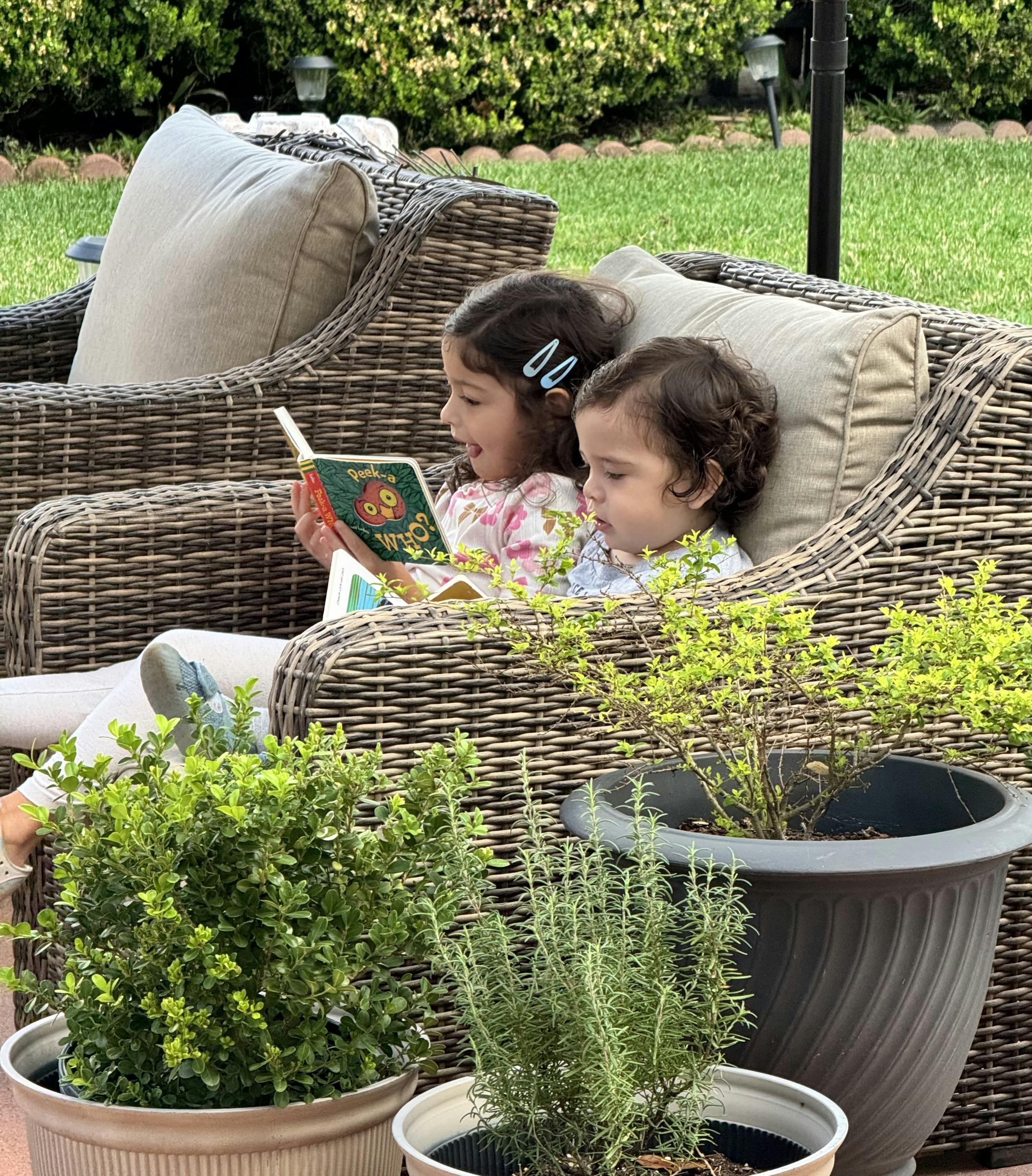 two children in wicker chairs reading a book outdoors