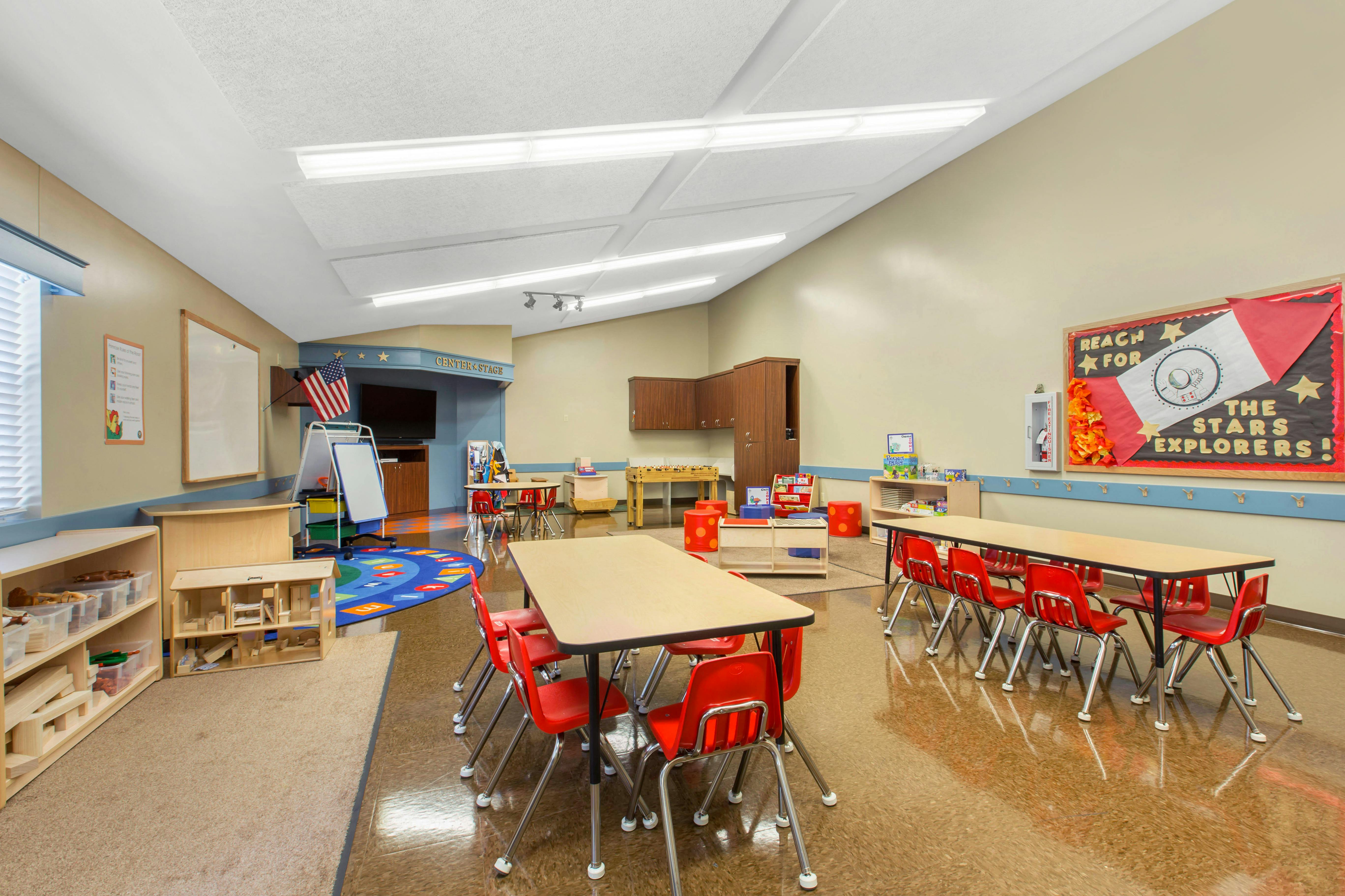 An empty children's classroom with several tables and red chairs