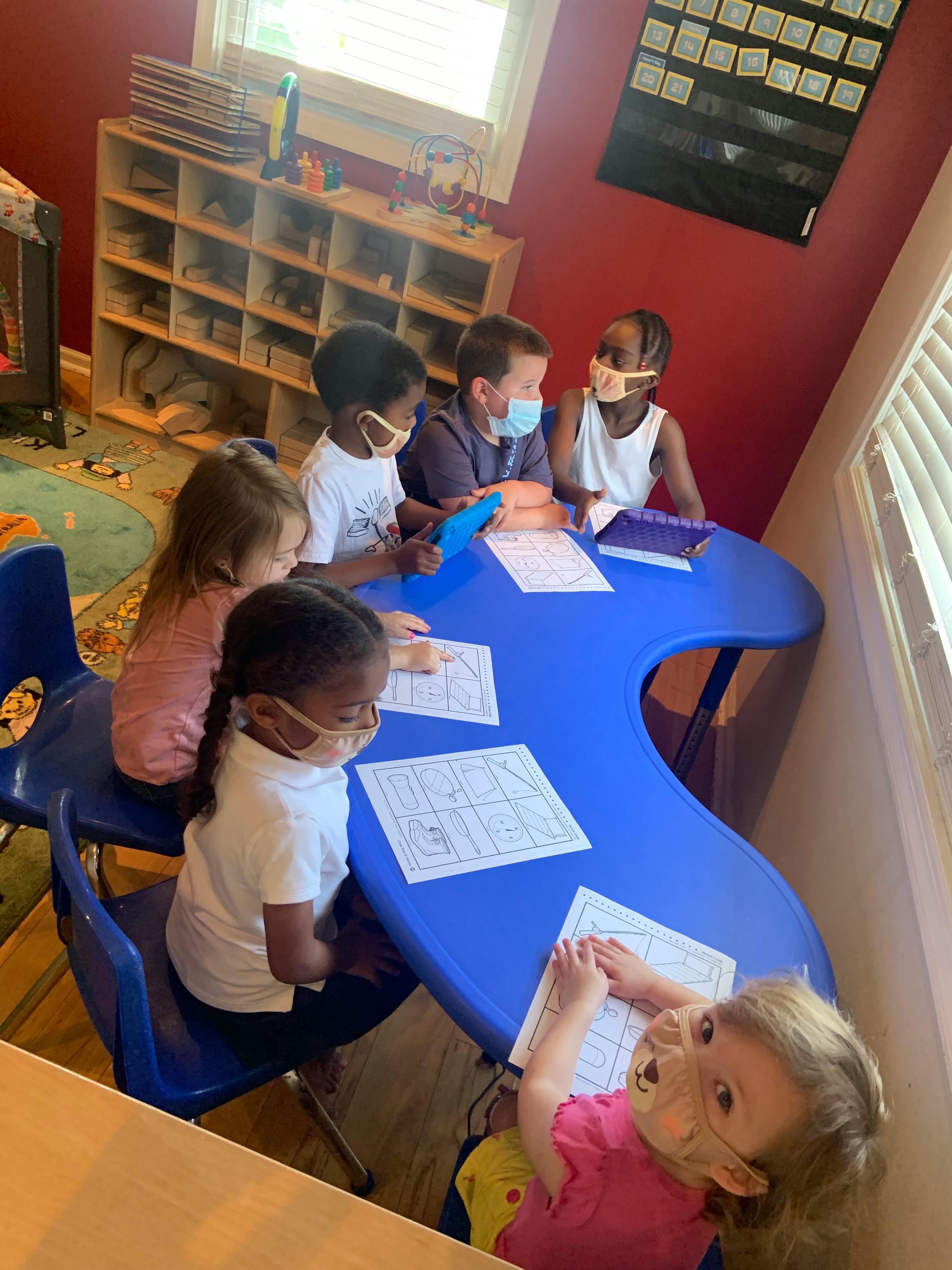 Children wearing masks sitting at a blue table with papers