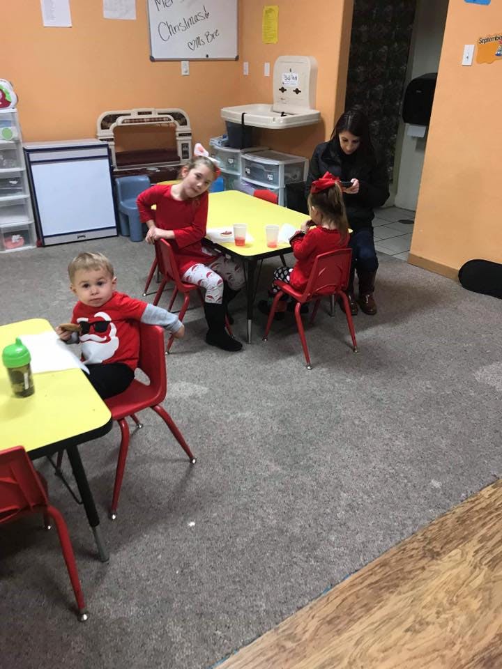 Three children and one person sitting at tables in a classroom
