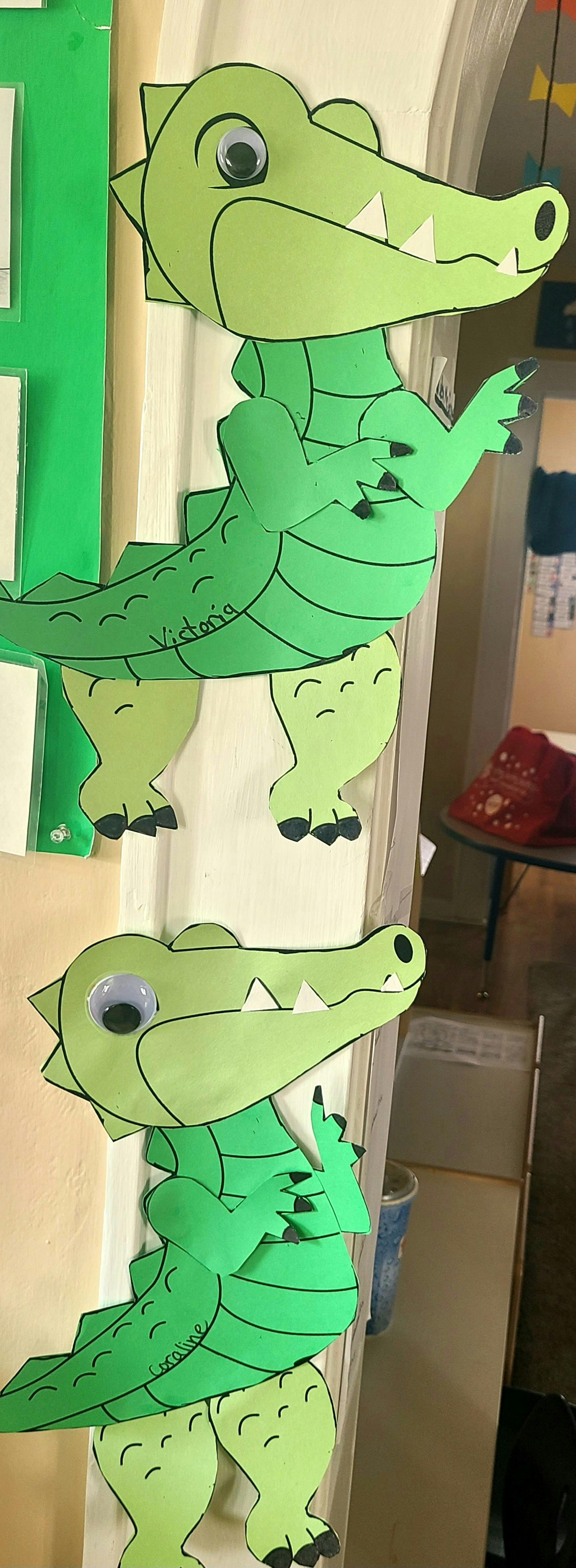 Two green paper alligator crafts with googly eyes