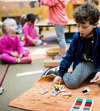 Child playing with colorful blocks on a mat in a classroom
