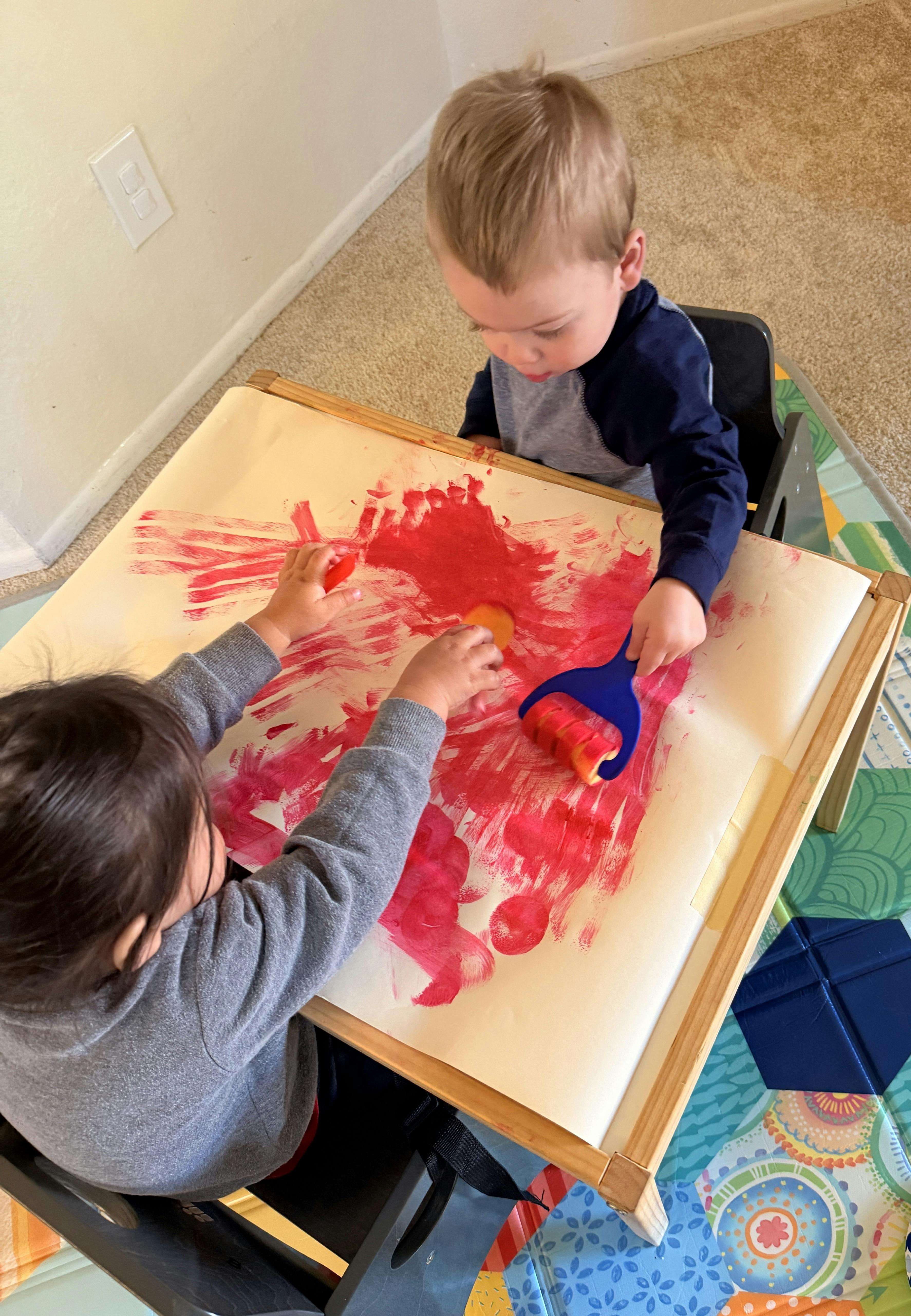 Two children painting with red paint on a large paper