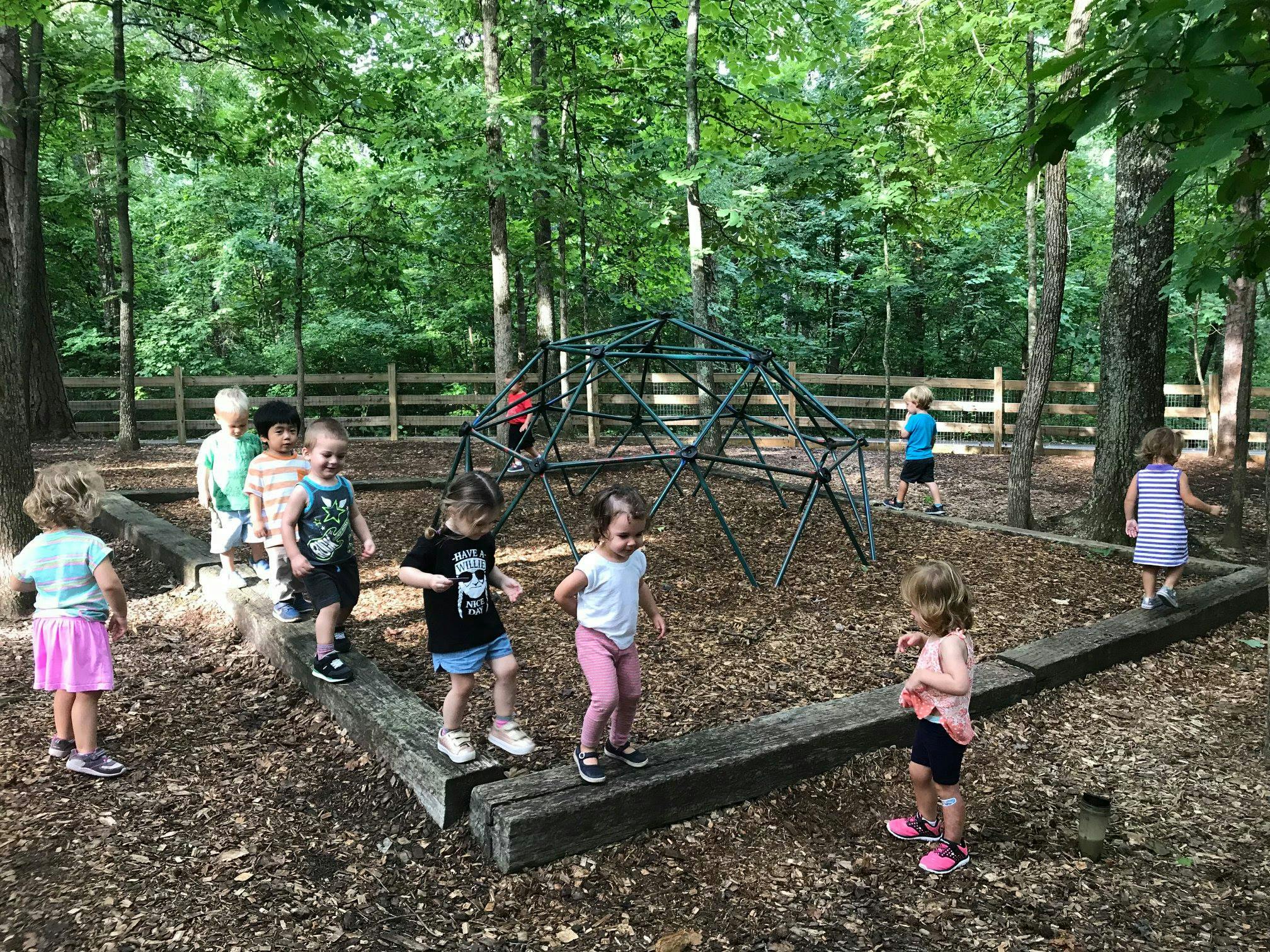 Children playing on wooden beams and a climbing dome in a wooded area