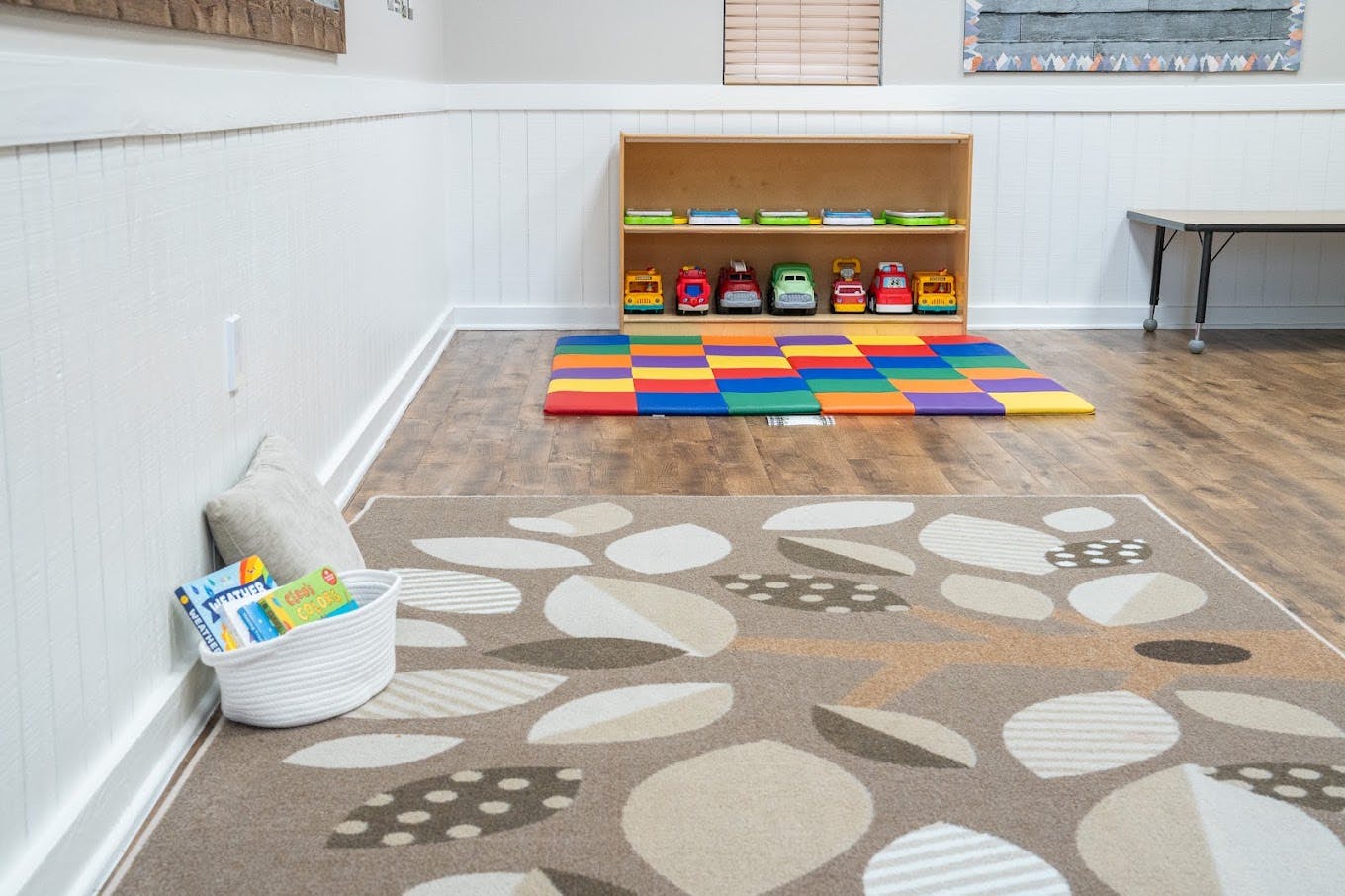 Childcare room with toy trucks on shelves and colorful play mats on the floor