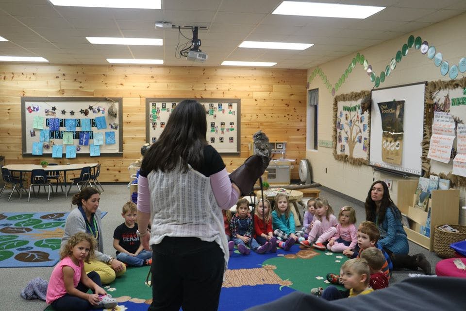 Person holding a bird on their arm in front of children in a classroom