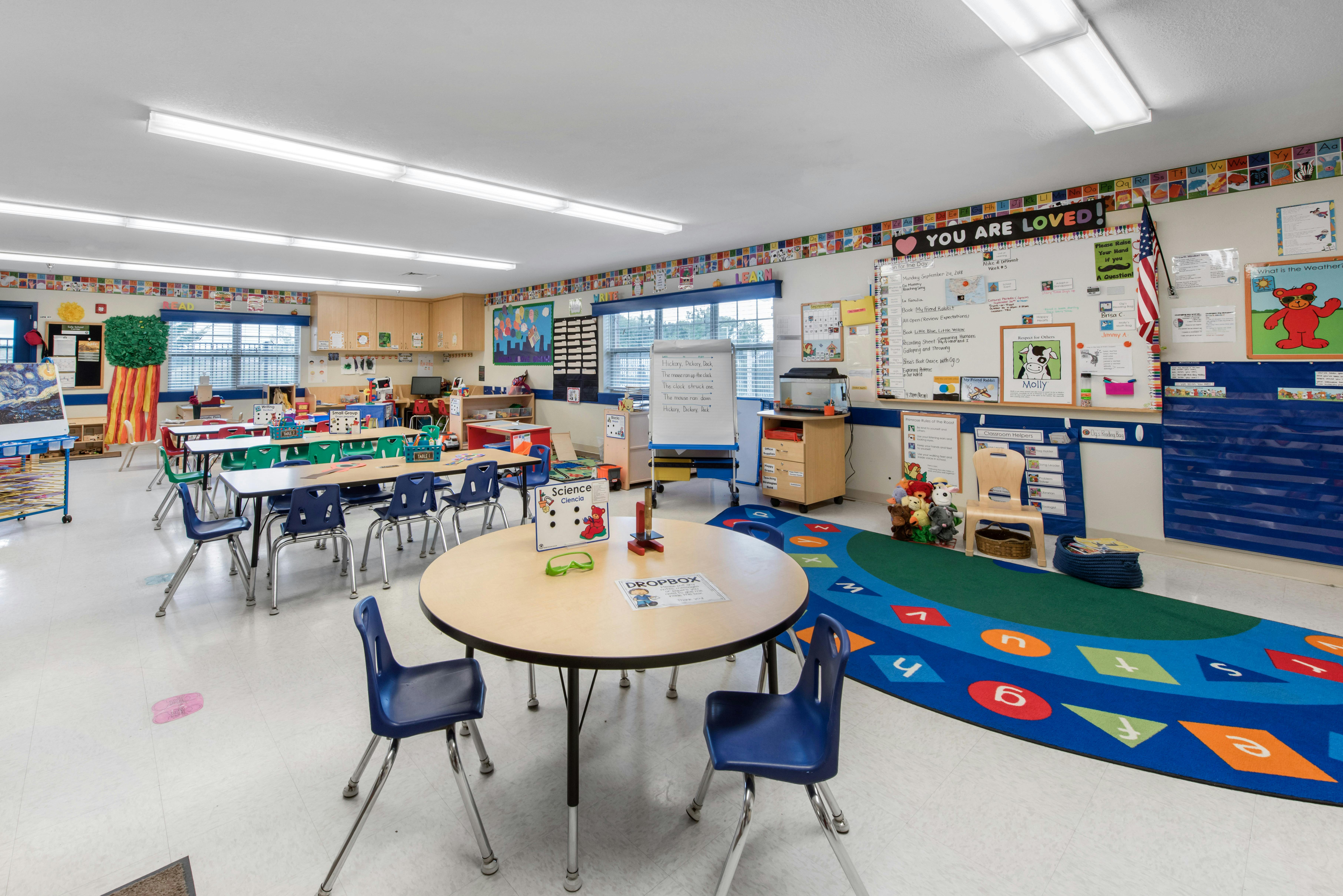 An empty, brightly lit classroom with small tables and chairs, and colorful decorations