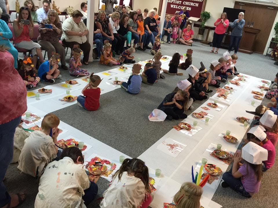 Children sitting on the floor around tables with adults watching