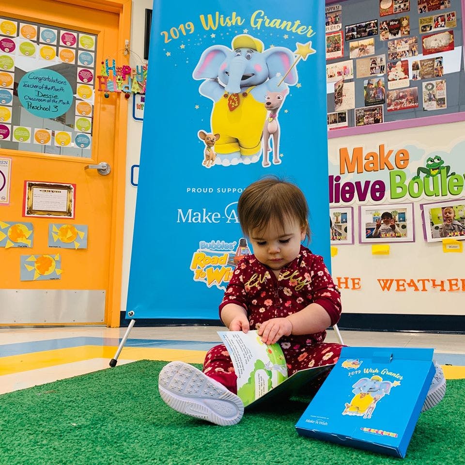 Child sitting on a green mat, looking at an open book