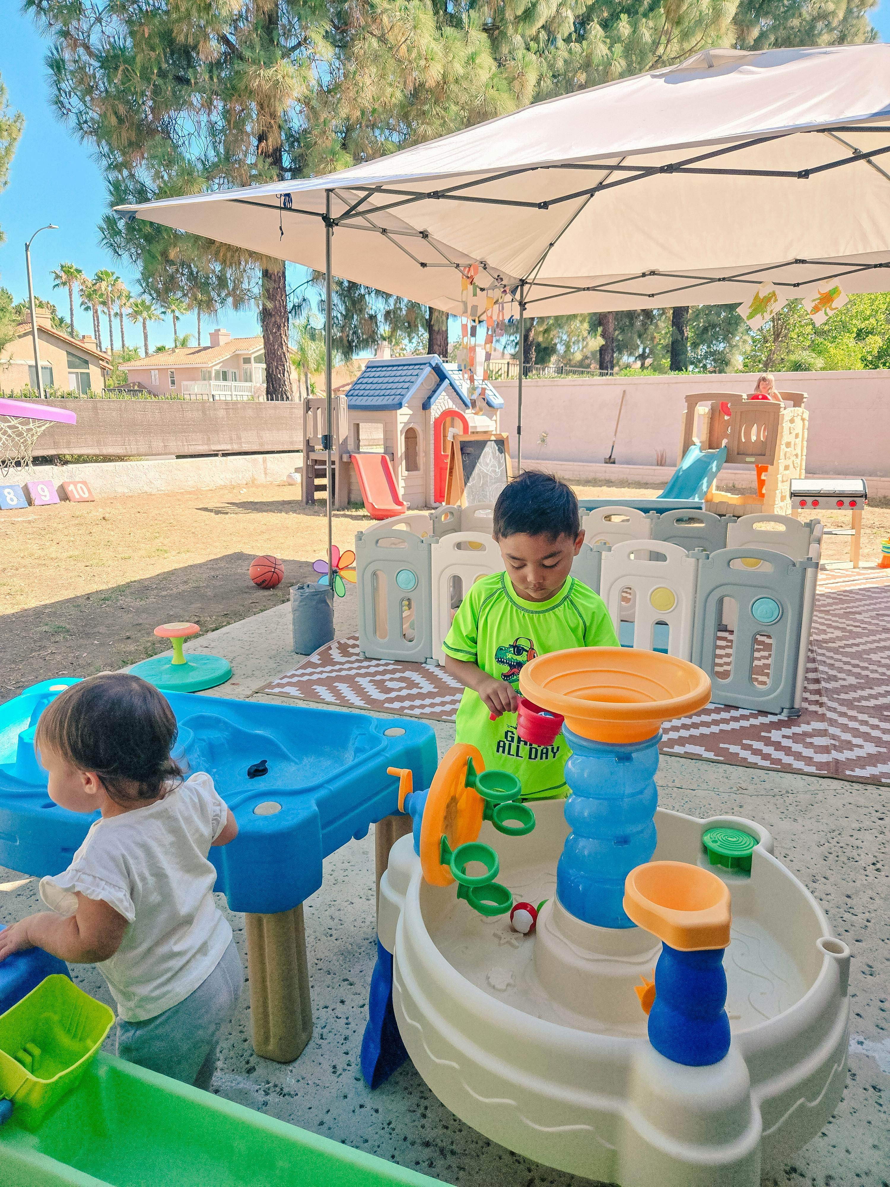 Children playing with a water table outdoors under a canopy
