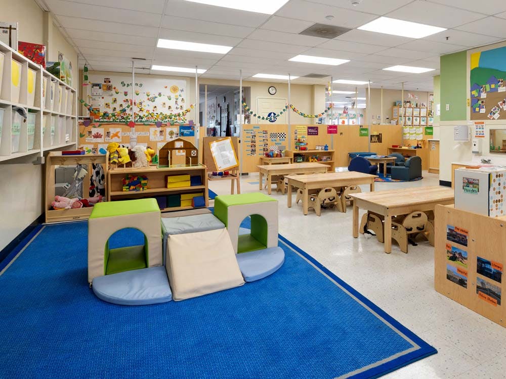An empty early childhood classroom with play mats, low tables, and shelves