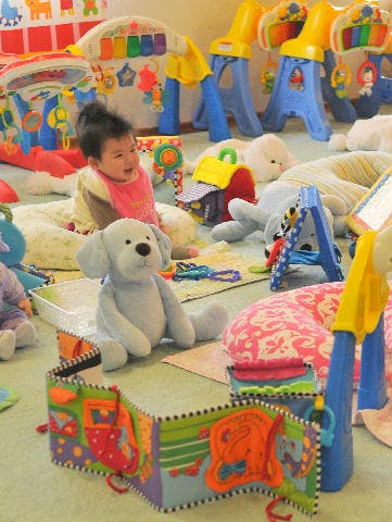 Child sitting on a mat surrounded by toys and a stuffed dog