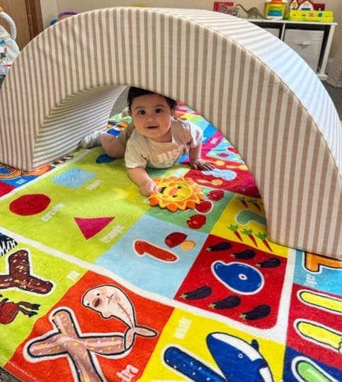 Child crawling under a striped arch on a colorful playmat