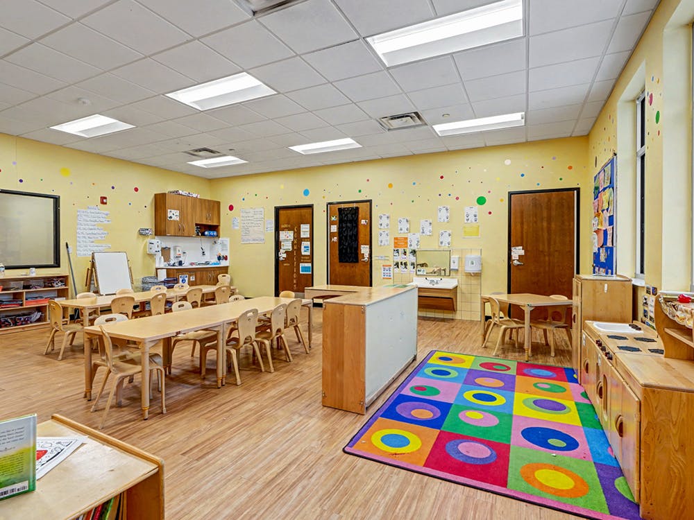 Empty classroom with small tables, chairs, and colorful rug