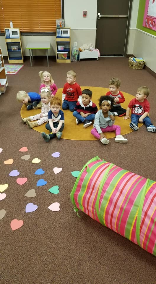 Children sitting on a yellow mat in a classroom