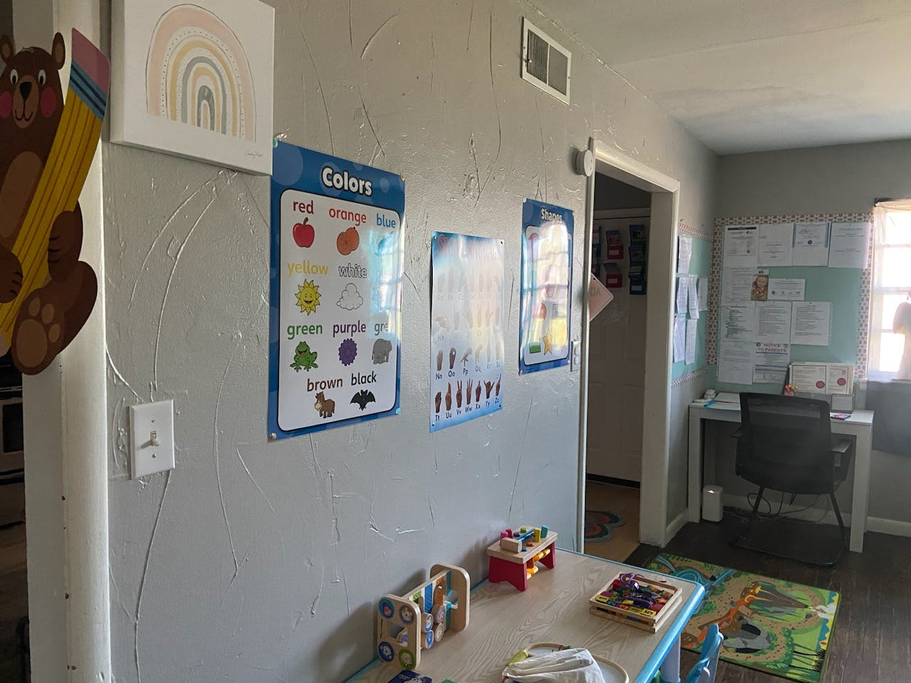 Wall with educational posters, small table with toys, and a desk