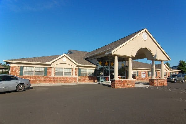 Building with brick and tan siding, a covered entrance, and parked cars